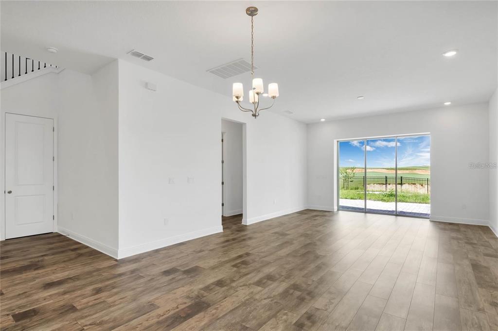 An empty room with wood-look flooring, a chandelier, and sliding glass doors to a yard — 15730 VETTA DRIVE, MONTVERDE, FL