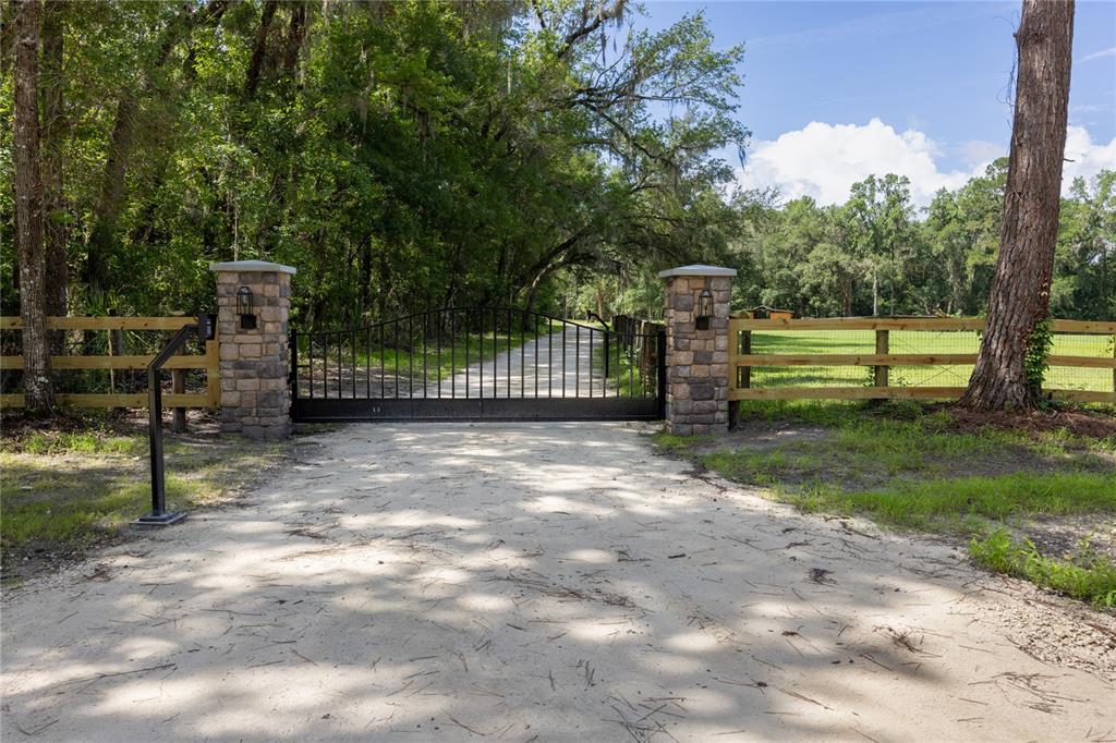 A black metal gate sits between two stone pillars at the entrance to a driveway — 14810 NW 185 STREET, WILLISTON, FL