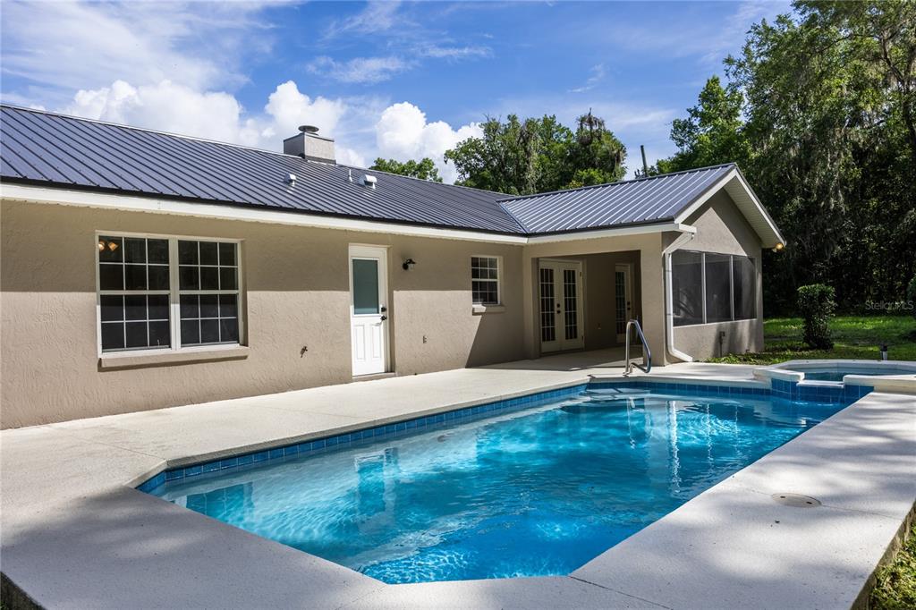 A backyard features a swimming pool with a spa adjacent to a tan house exterior — 14810 NW 185 STREET, WILLISTON, FL