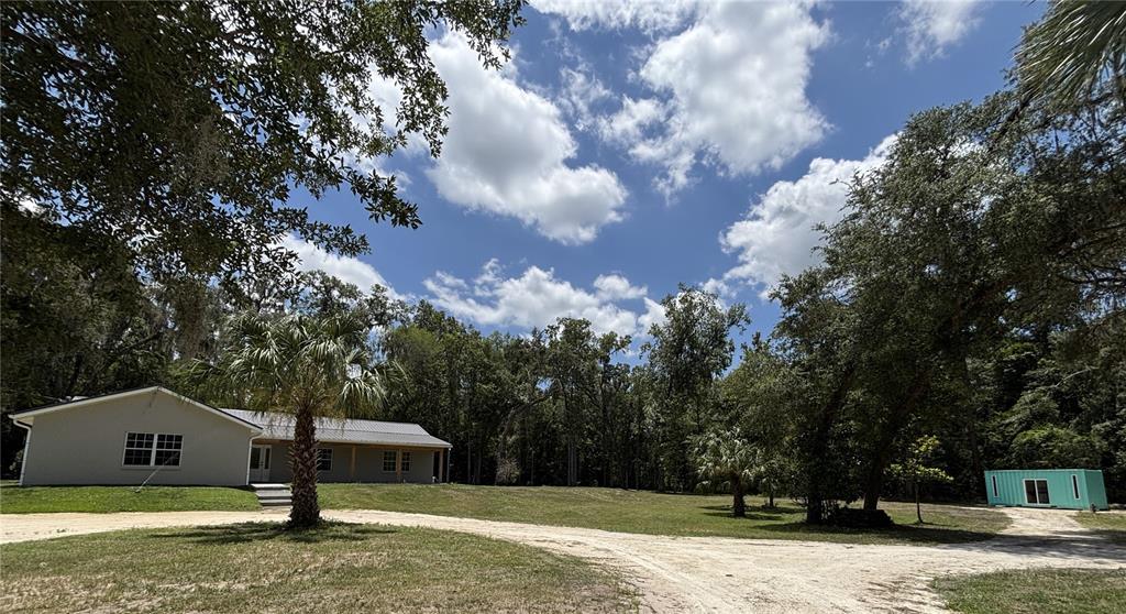 A light-colored house with a metal roof sits on a grassy lot with trees — 14810 NW 185 STREET, WILLISTON, FL