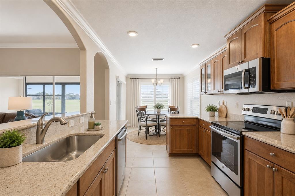A kitchen with wood cabinets, granite countertops, and stainless steel appliances overlooks a dining area — 27143 ROANOKE DRIVE, LEESBURG, FL