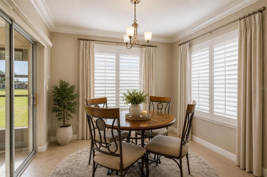 A dining area features a round wooden table, four chairs, plantation shutters, and sliding doors — 27143 ROANOKE DRIVE, LEESBURG, FL
