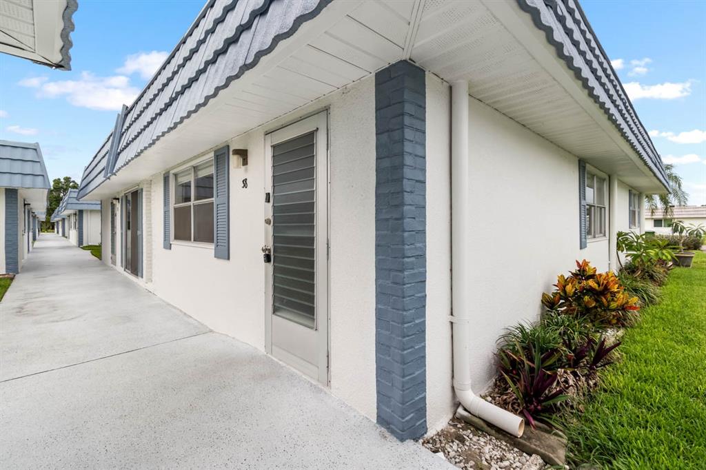 A white exterior building with blue accents, a concrete walkway, and a small garden area — 1901 ANDOVER WAY UNIT 38, SUN CITY CENTER, FL