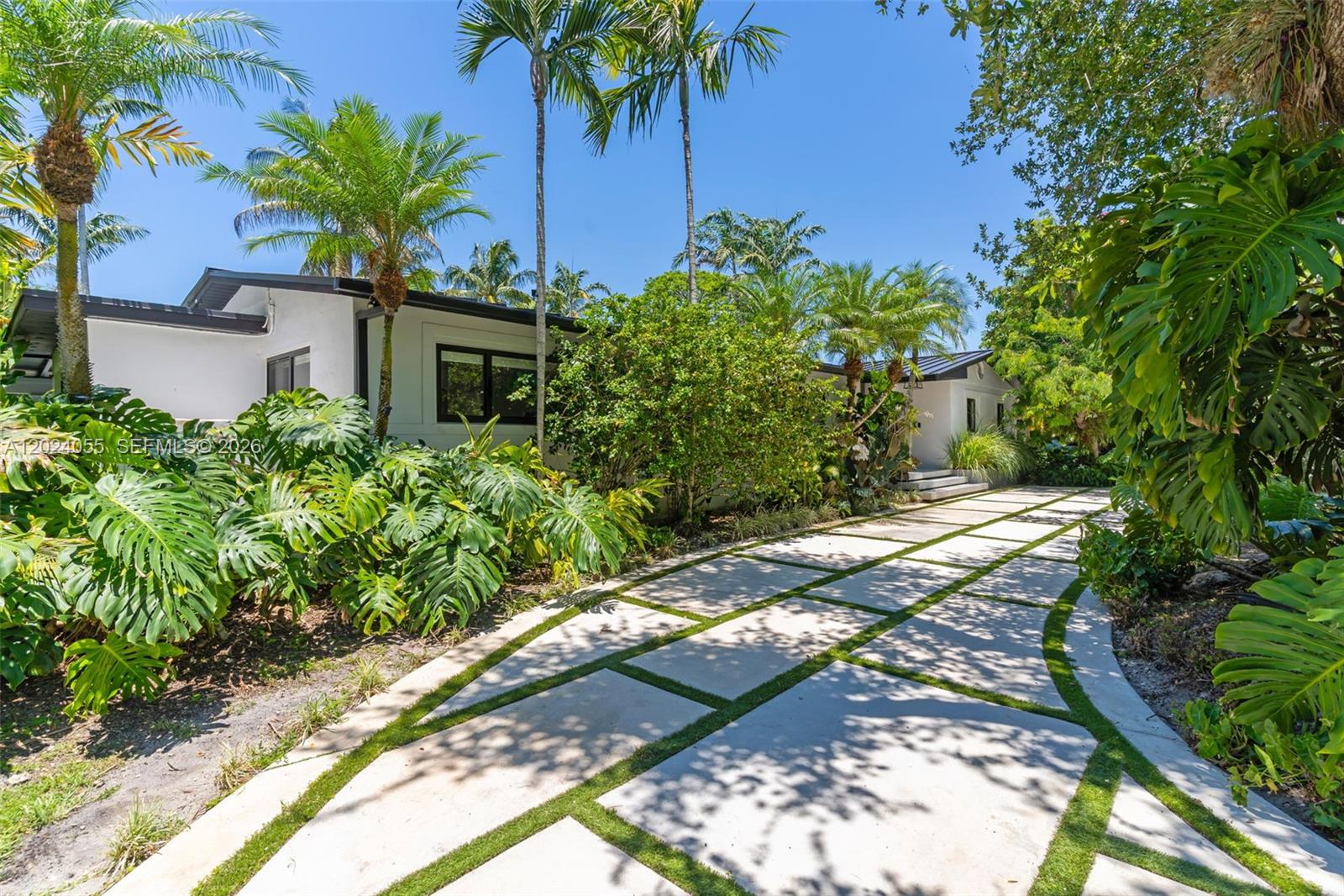 A white house with a modern grid-patterned driveway is surrounded by lush tropical landscaping — 13400 SW 70th Ave, Pinecrest FL 33156, PINECREST, FL