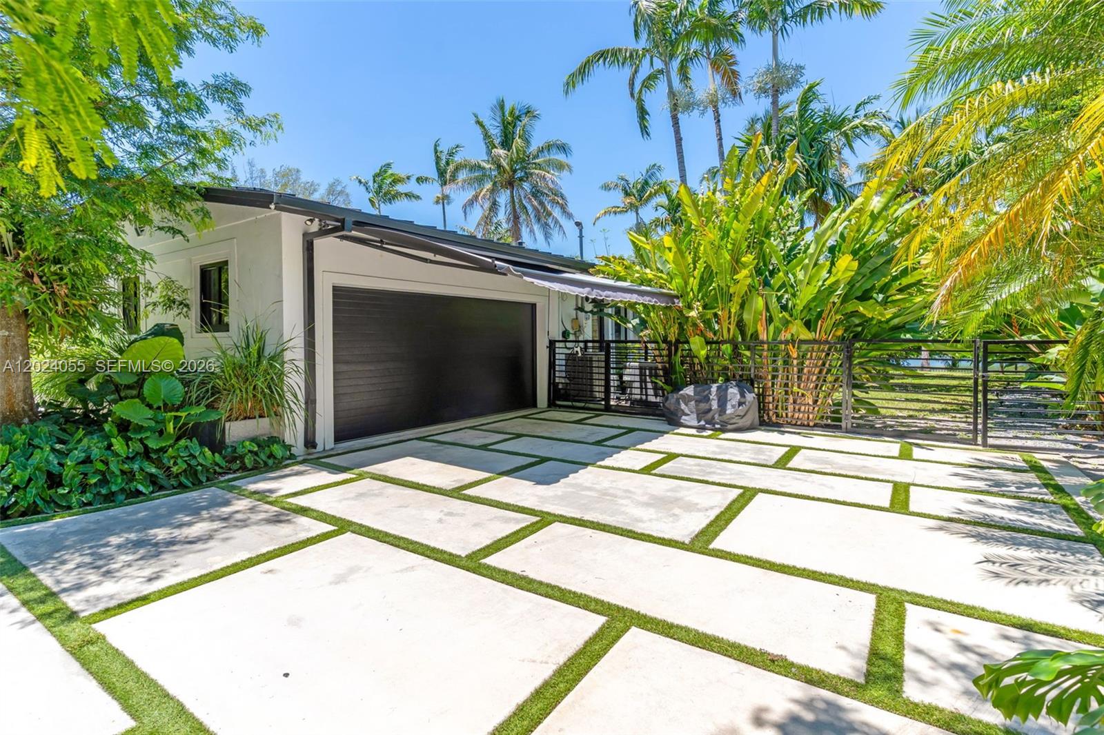 A modern home exterior features a dark garage door and a concrete paver driveway — 13400 SW 70th Ave, Pinecrest FL 33156, PINECREST, FL