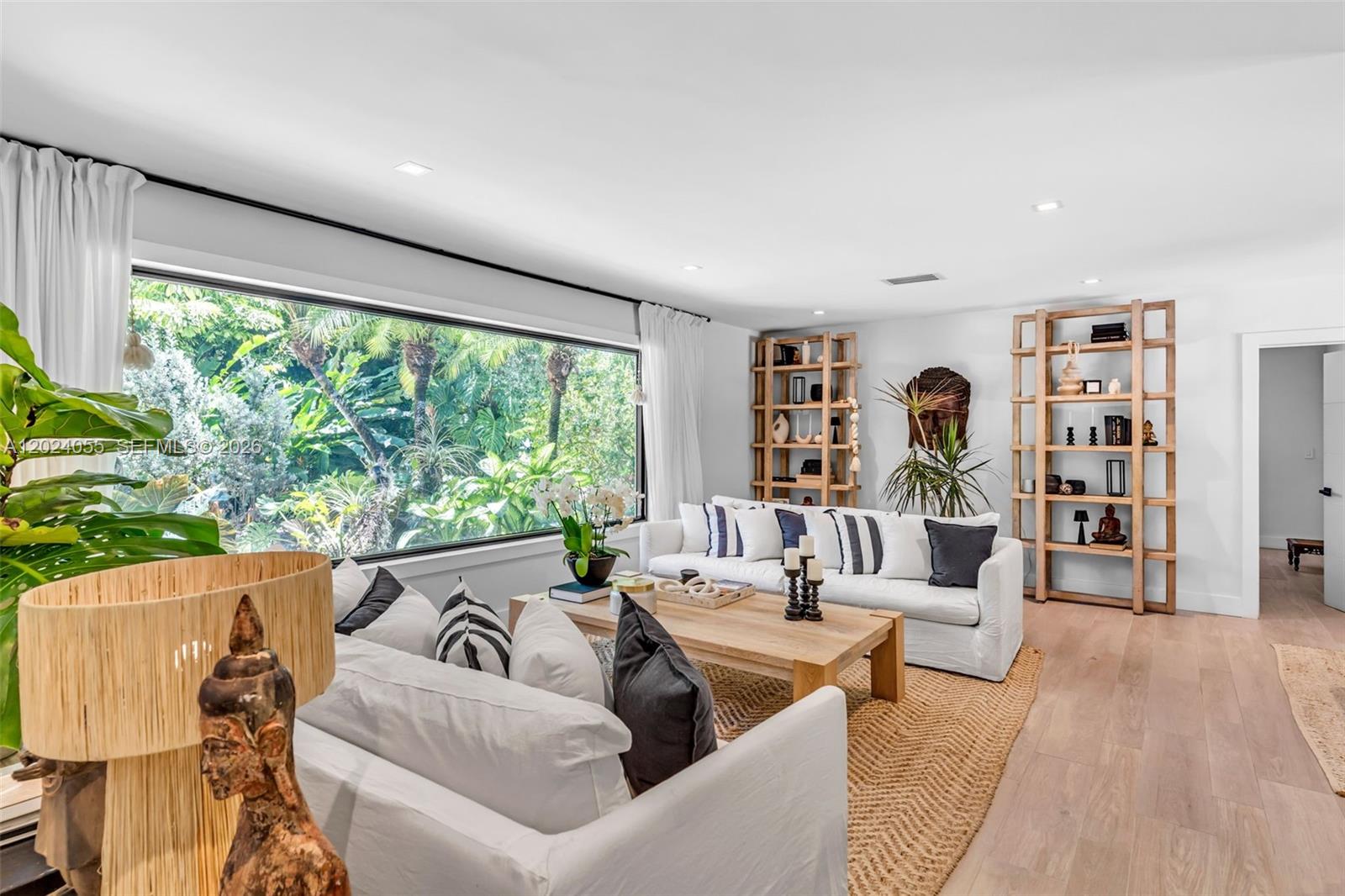 A living room features white sofas, wooden shelving, a coffee table, and a large window — 13400 SW 70th Ave, Pinecrest FL 33156, PINECREST, FL