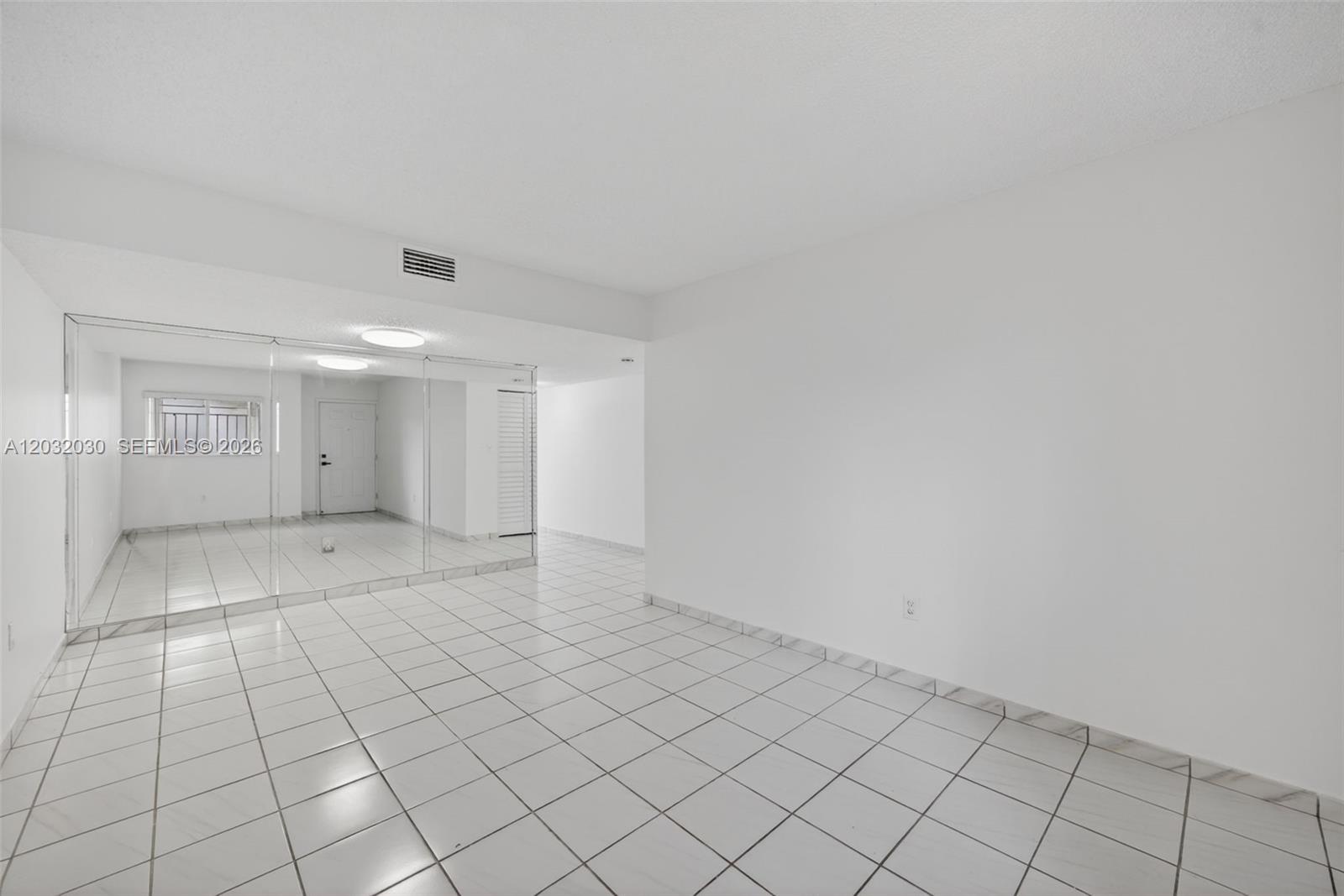 An empty room features white tiled floors, plain white walls, and a large mirrored wall — 800 SW 104th Ct # 103, Miami FL 33174, MIAMI, FL