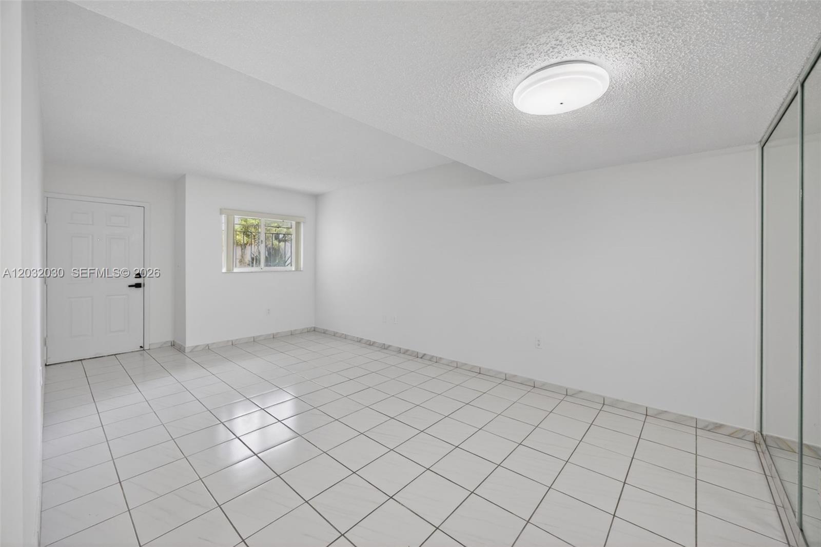 An empty room features white tiled floors, white walls, a ceiling light, and mirrored closet doors — 800 SW 104th Ct # 103, Miami FL 33174, MIAMI, FL