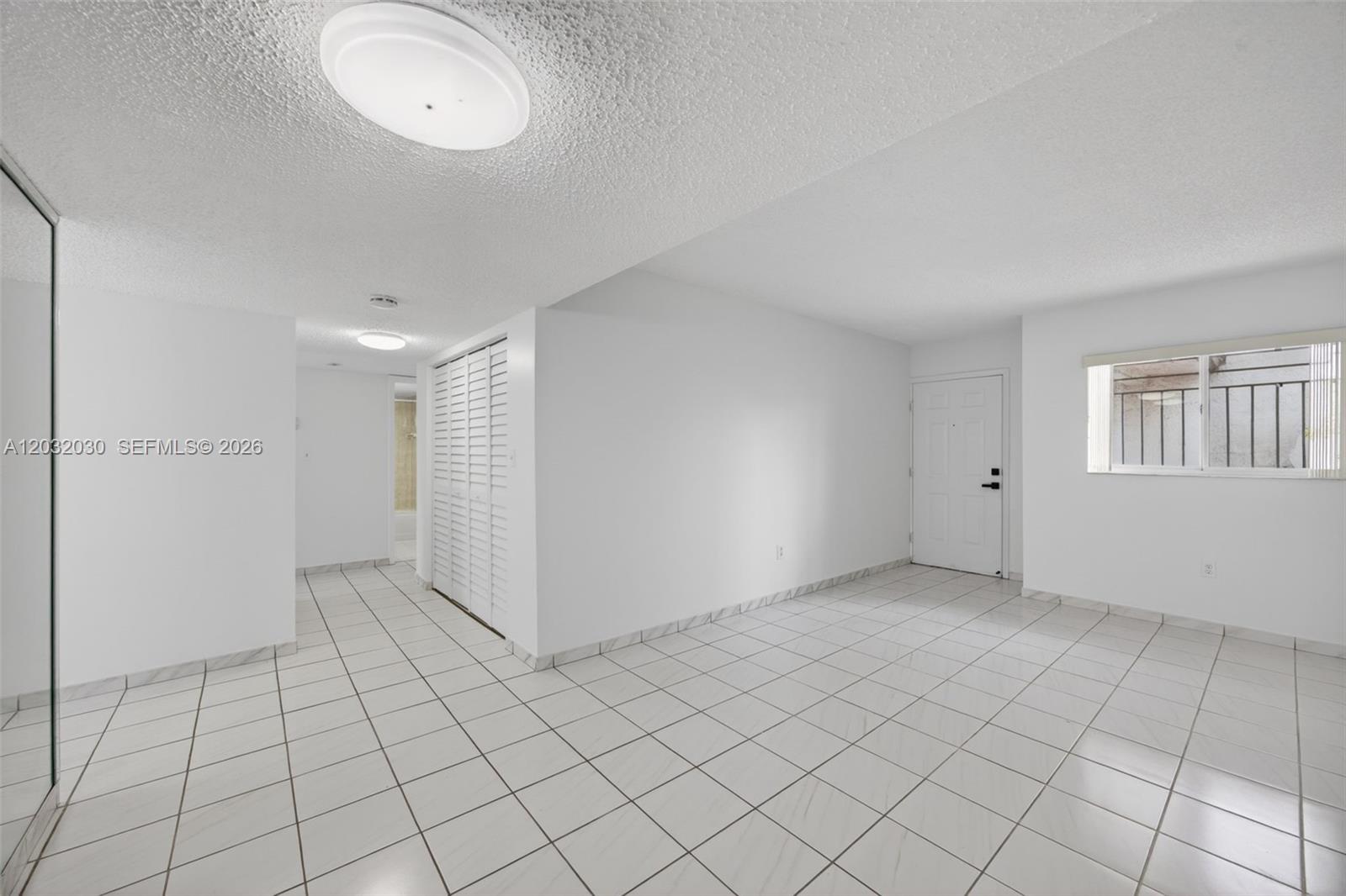 An empty room features white tiled floors, white walls, a closet, and a front door — 800 SW 104th Ct # 103, Miami FL 33174, MIAMI, FL