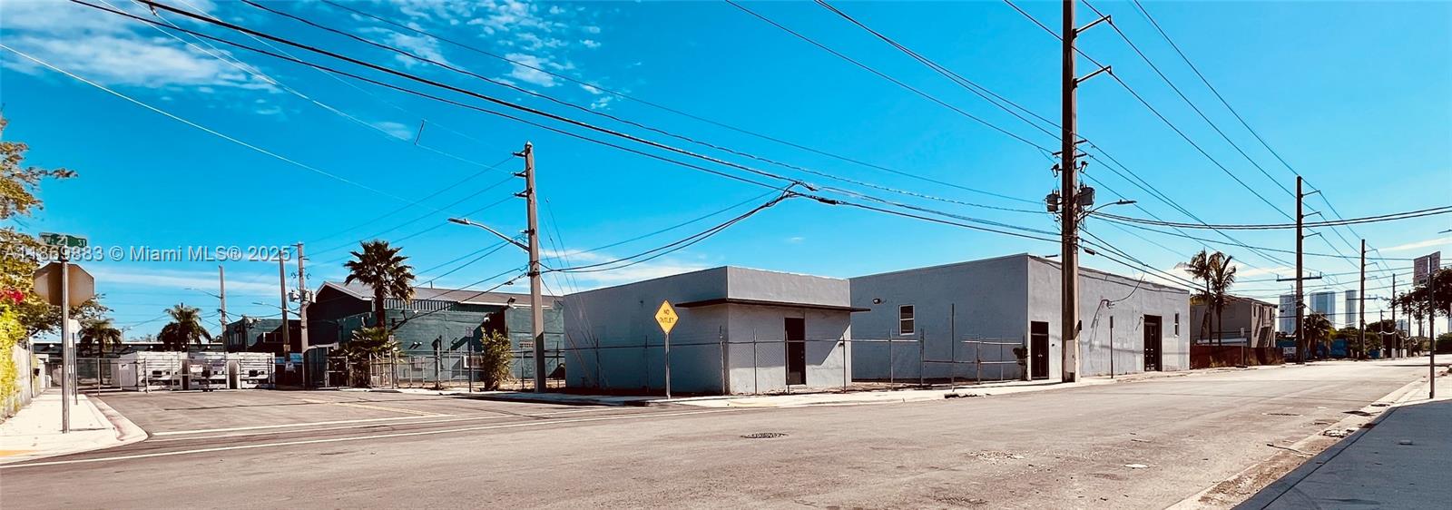 A street-level view shows two gray industrial buildings behind a chain-link fence under a blue sky — 1031 NW 21st St, Miami FL 33127, MIAMI, FL