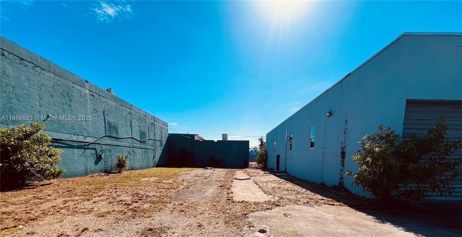 An outdoor alleyway sits between two painted concrete block buildings with a patch of dirt — 1031 NW 21st St, Miami FL 33127, MIAMI, FL