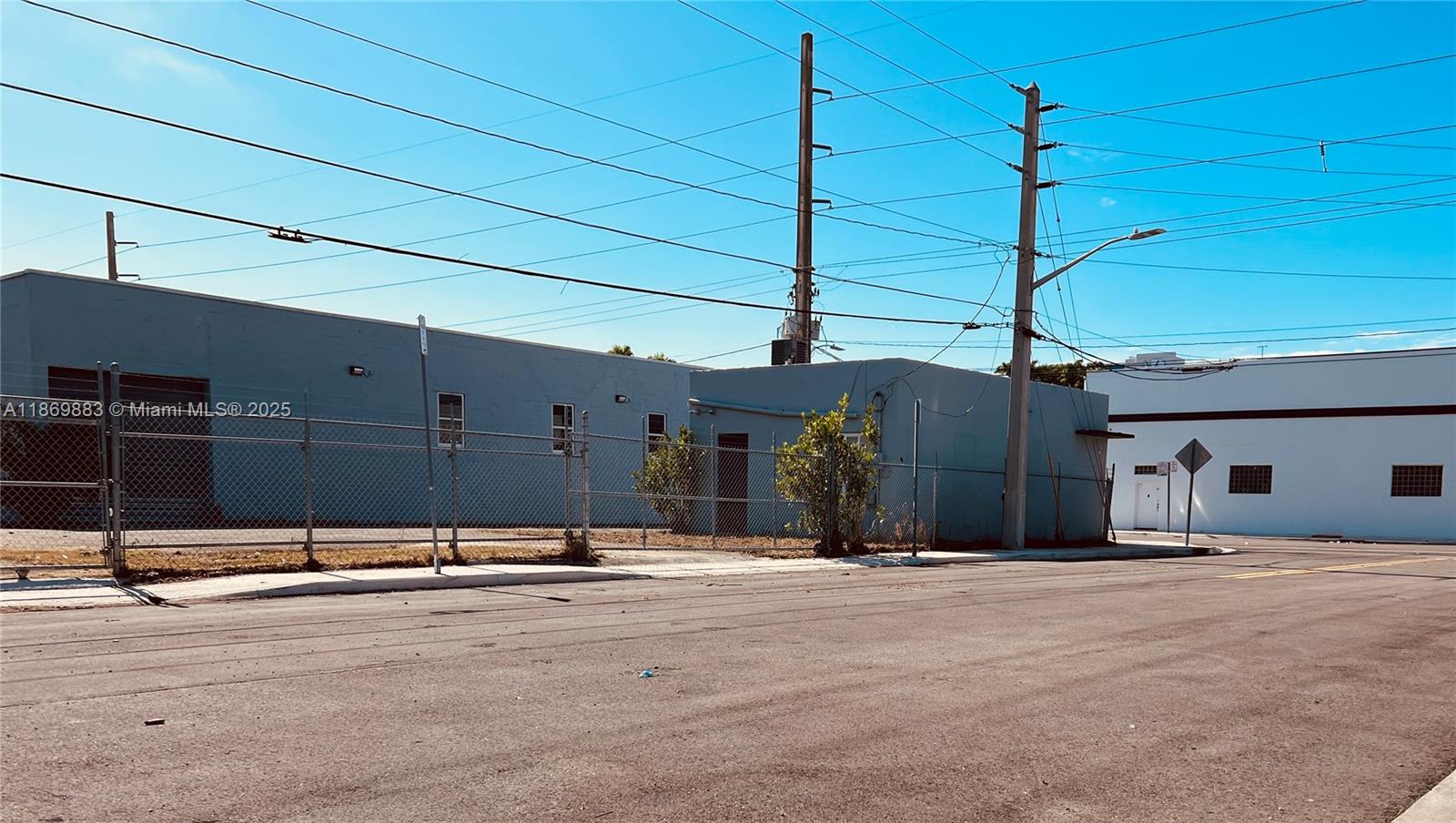 A view of a low-rise commercial building with a chain-link fence and utility poles — 1031 NW 21st St, Miami FL 33127, MIAMI, FL