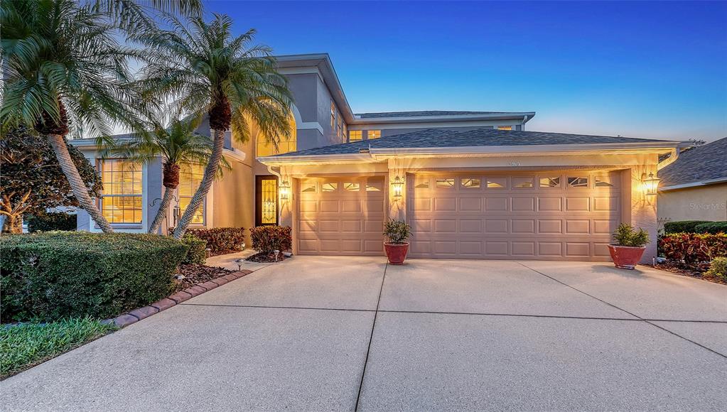 A two-story house with a three-car garage, palm trees, and a concrete driveway at dusk — 7915 KAVANAGH COURT, SARASOTA, FL