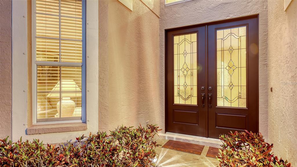 A front entryway features double dark wood doors with glass inserts beside a large window — 7915 KAVANAGH COURT, SARASOTA, FL