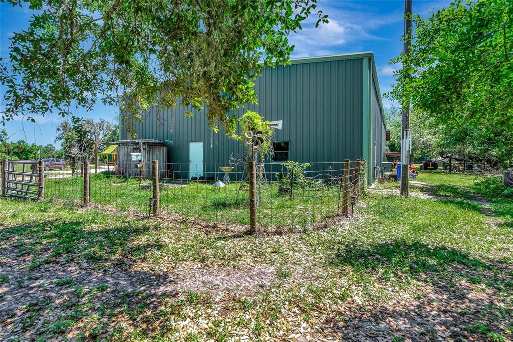 A green metal building stands behind a wire fence in a grassy, tree-shaded yard — 15750 WILSON ROAD, SARASOTA, FL