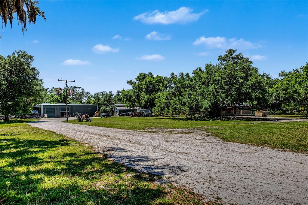 A gravel driveway leads toward a metal workshop and a house surrounded by large trees — 15750 WILSON ROAD, SARASOTA, FL