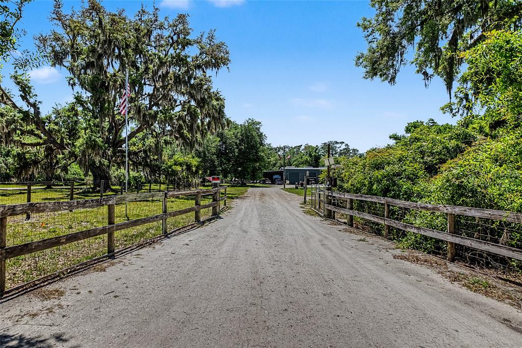 A dirt driveway leads toward a metal building framed by wooden fences and large trees — 15750 WILSON ROAD, SARASOTA, FL