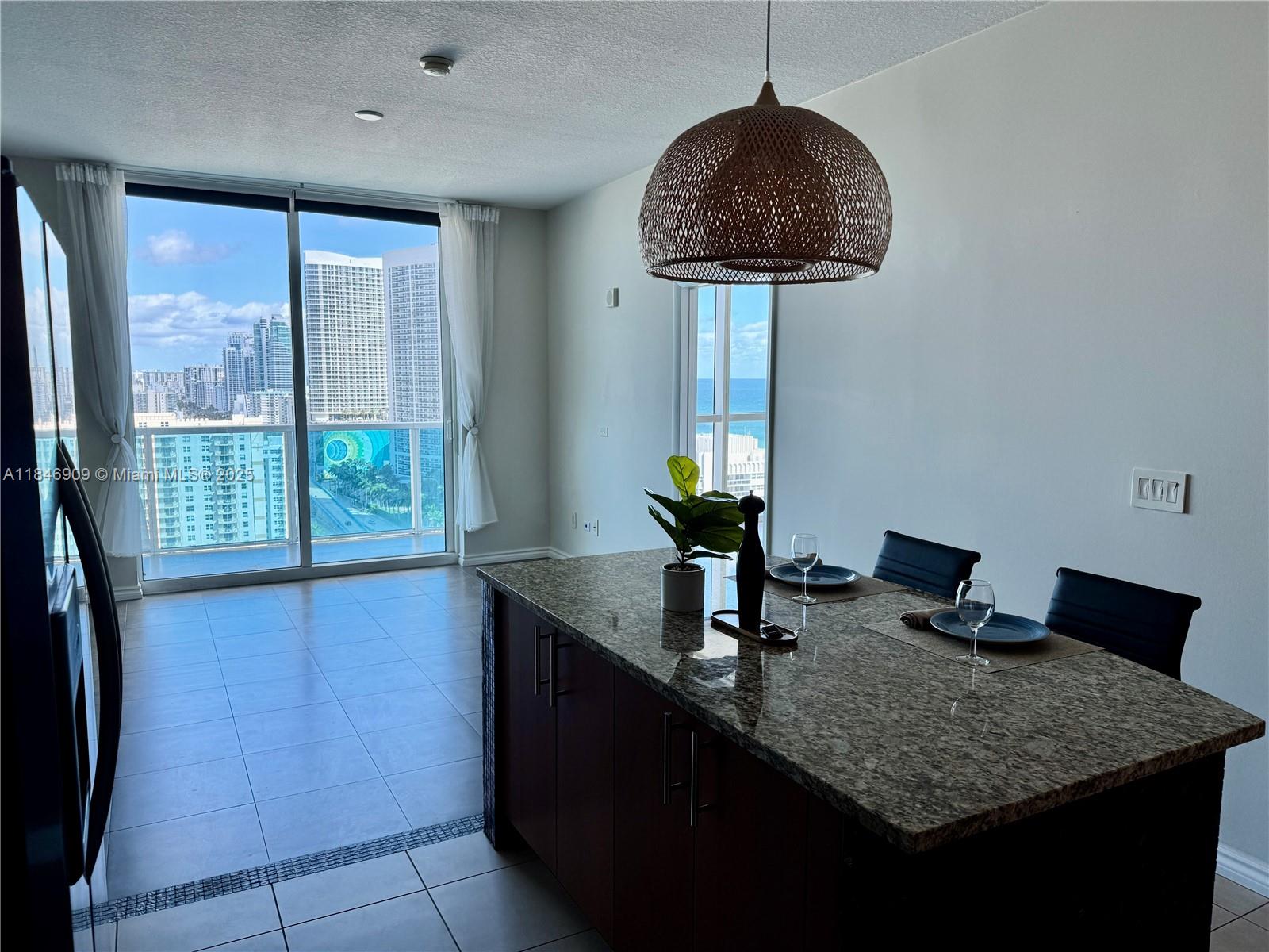 A kitchen island with granite countertops sits in a room featuring floor-to-ceiling city views — 1945 S Ocean Dr # 2311, Hallandale Beach FL 33009, HALLANDALE BEACH, FL