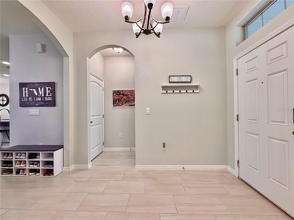 An entryway features tile flooring, a white front door, a shoe rack, and an arched hallway — 17098 WATER SPRING BOULEVARD, WINTER GARDEN, FL