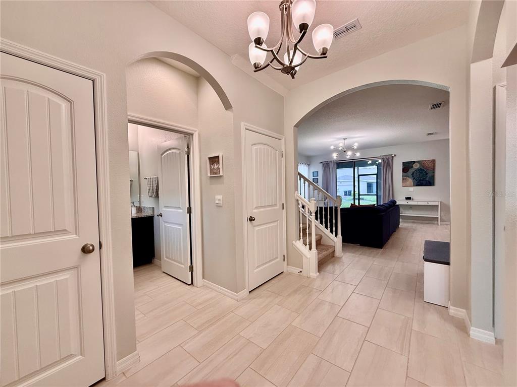 An entryway with light tile flooring leads to a staircase and a living area beyond — 17098 WATER SPRING BOULEVARD, WINTER GARDEN, FL