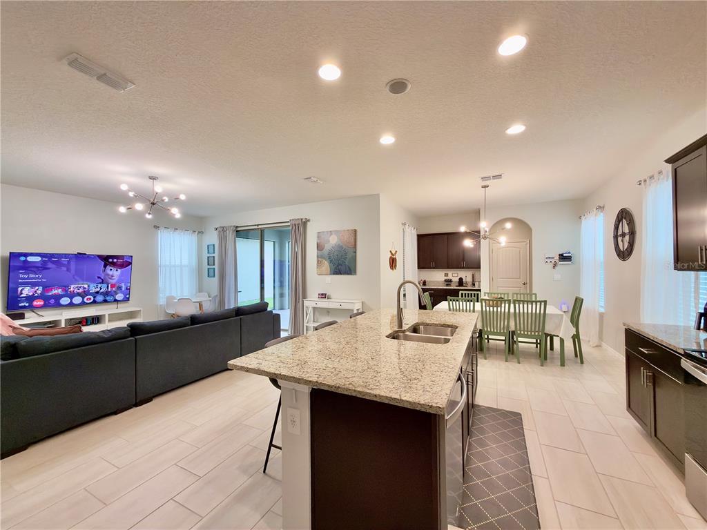 An open-concept kitchen with a granite island overlooks a living room and dining area — 17098 WATER SPRING BOULEVARD, WINTER GARDEN, FL