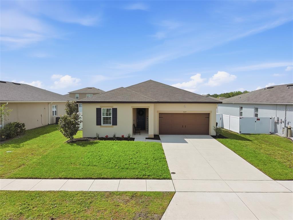 A single-story suburban house features a tan exterior, a brown garage door, and a front lawn — 5629 WESTERN SUN DRIVE, ST CLOUD, FL
