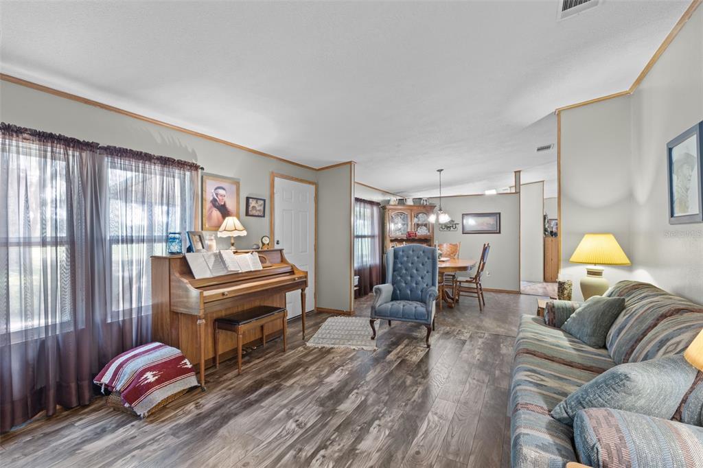 A living room features wood-look flooring, a piano, a blue armchair, and a striped sofa — 6689 SE 55TH STREET, TRENTON, FL