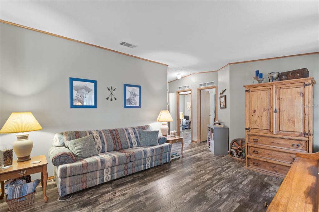 A living room features a patterned sofa, wood-look flooring, and a large wooden armoire — 6689 SE 55TH STREET, TRENTON, FL