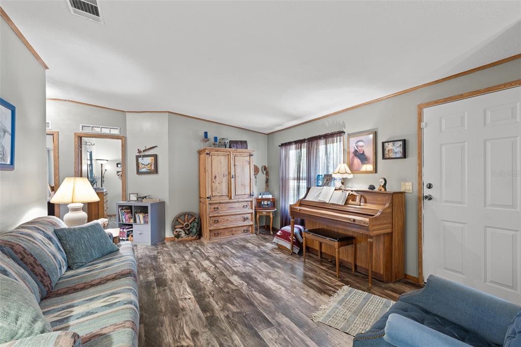 A living room features wood-look flooring, a piano, a wooden armoire, and a patterned sofa — 6689 SE 55TH STREET, TRENTON, FL