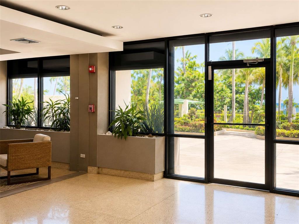 A bright lobby features floor-to-ceiling windows, potted plants, tiled flooring, and a glass door — 4745 AVE ISLA VERDE UNIT 4-D, CAROLINA, PR