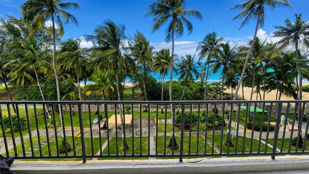 A balcony view overlooking a grassy courtyard, palm trees, and a sandy beach with ocean — 4745 AVE ISLA VERDE UNIT 4-D, CAROLINA, PR