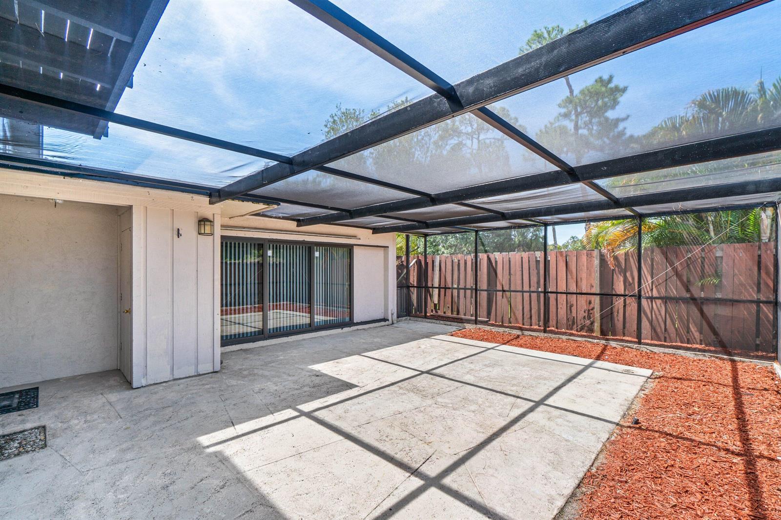 A screened-in concrete patio features a sliding glass door and a wooden privacy fence — 4585 Holly Lake Drive, Lake Worth FL 33463, LAKE WORTH, FL