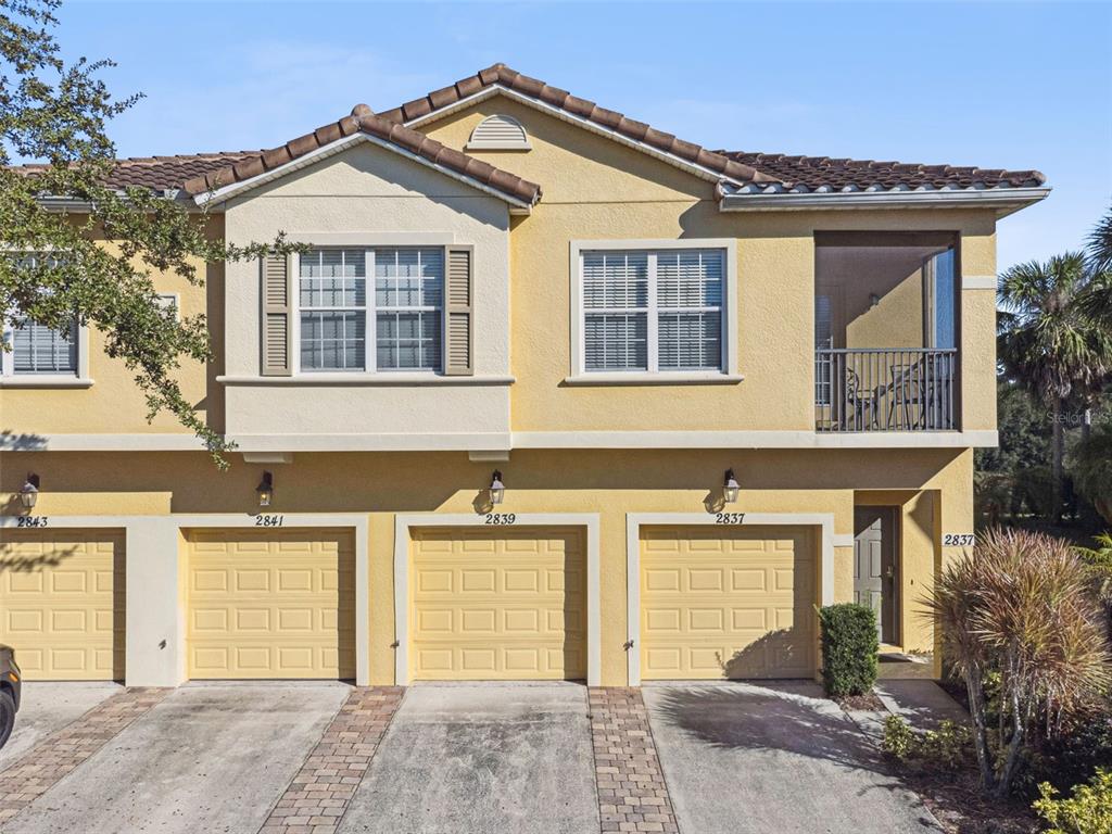 An exterior view of a multi-unit townhouse building with yellow stucco walls and garage doors — 2841 OAKWATER DRIVE, KISSIMMEE, FL