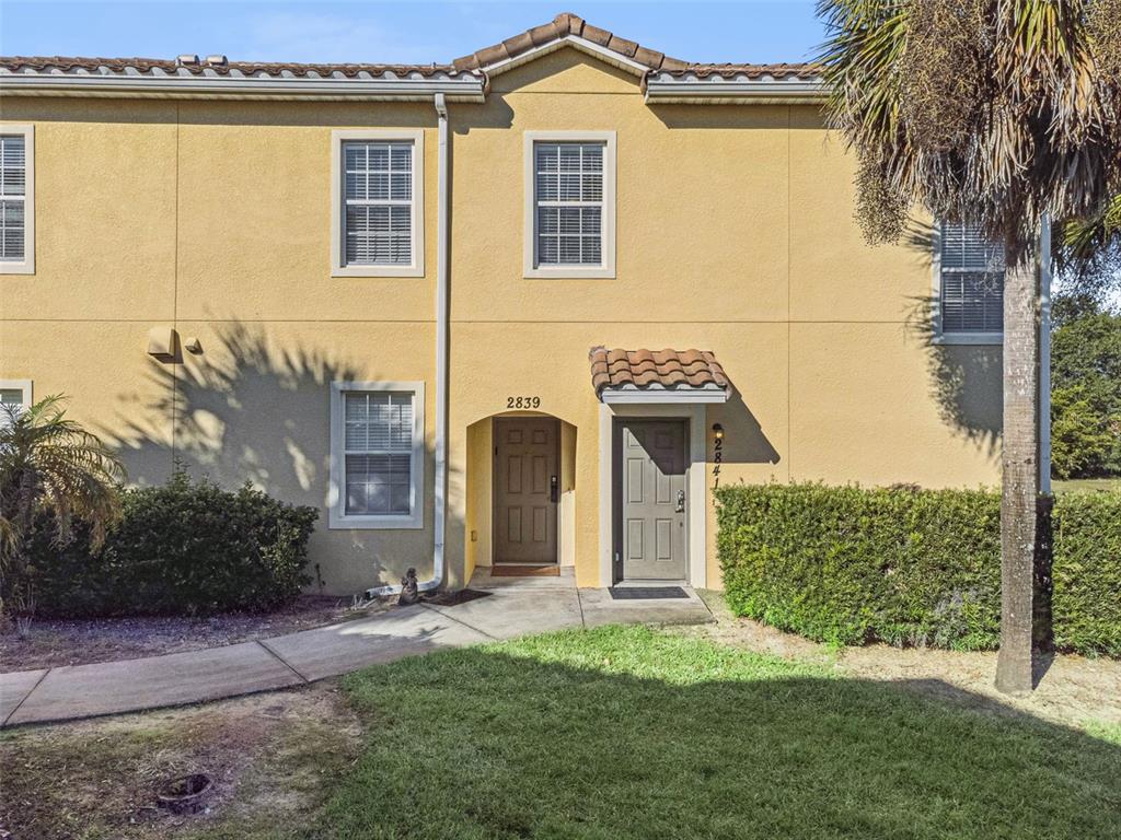 A two-story yellow stucco townhouse exterior features two front doors and a tiled roof — 2841 OAKWATER DRIVE, KISSIMMEE, FL