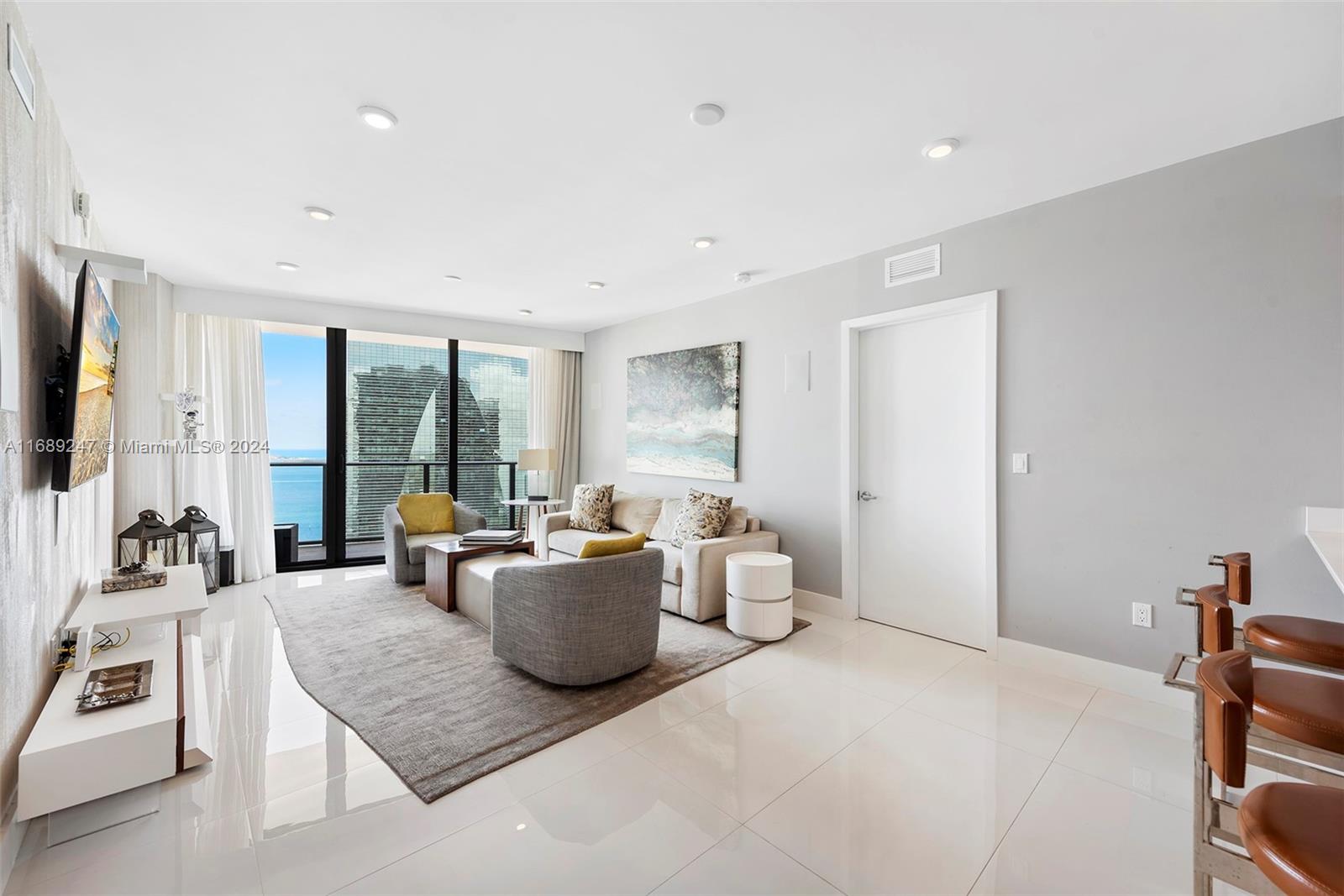 A modern living room features white tile floors, a neutral sofa, and floor-to-ceiling ocean views — 1300 S Miami Ave # 3402, Miami FL 33130, MIAMI, FL