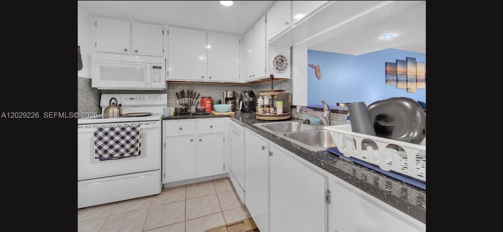 A kitchen features white cabinets, dark countertops, a tiled backsplash, and white appliances — 9427 NW 42nd St, Sunrise FL 33351, SUNRISE, FL