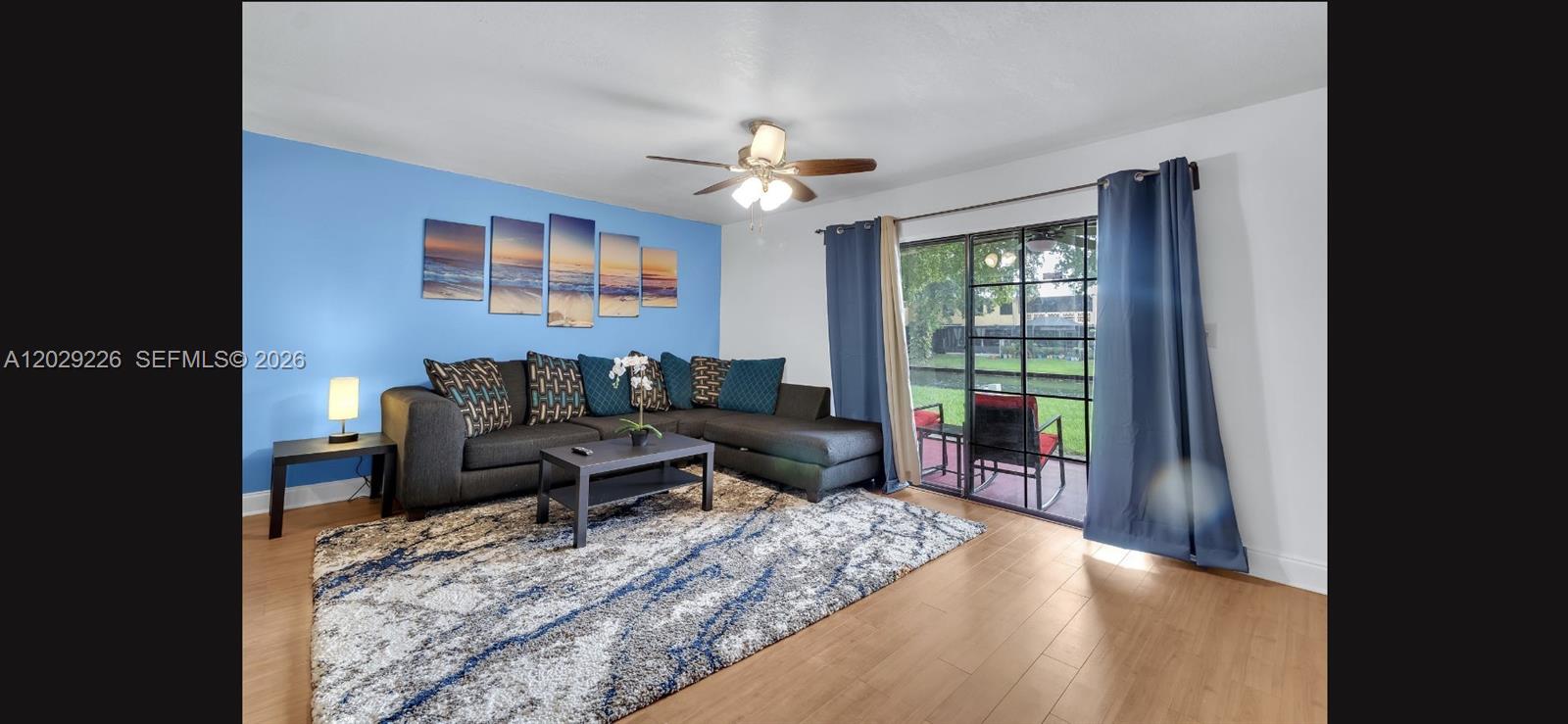 A living room features a blue accent wall, a sectional sofa, and a sliding glass door — 9427 NW 42nd St, Sunrise FL 33351, SUNRISE, FL