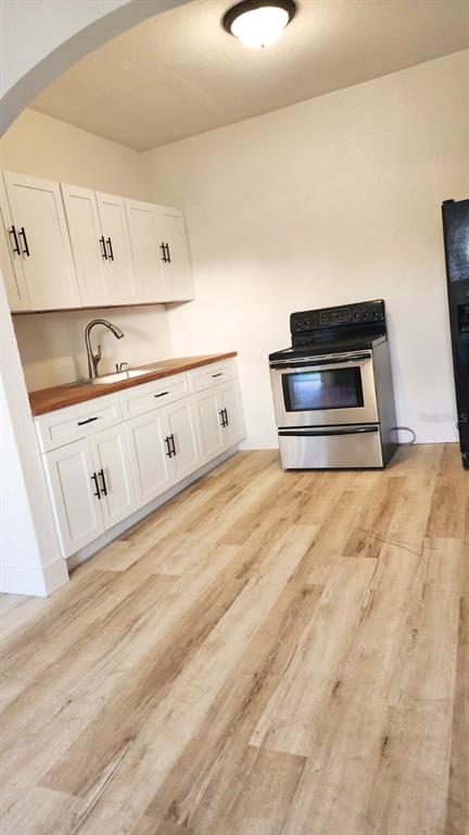 A kitchen features white cabinets, wood countertops, a stainless steel stove, and light wood flooring — 412 BAY STREET NW, FORT MEADE, FL