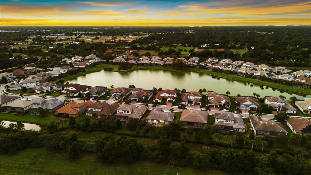 An aerial view shows a suburban neighborhood with houses surrounding a central lake at sunset — 6325 RIVO LAKES BOULEVARD, SARASOTA, FL