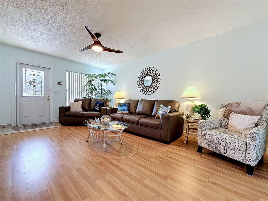 A living room features wood-look flooring, a brown leather sofa, and a patterned accent chair — 11935 BOYNTON LANE UNIT 17GB, NEW PORT RICHEY, FL