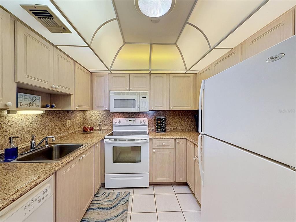A kitchen features light wood cabinets, granite countertops, white appliances, and a vaulted ceiling — 11935 BOYNTON LANE UNIT 17GB, NEW PORT RICHEY, FL