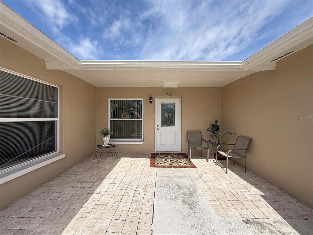 A covered patio features light-colored pavers, two chairs, a small table, and a white door — 11935 BOYNTON LANE UNIT 17GB, NEW PORT RICHEY, FL