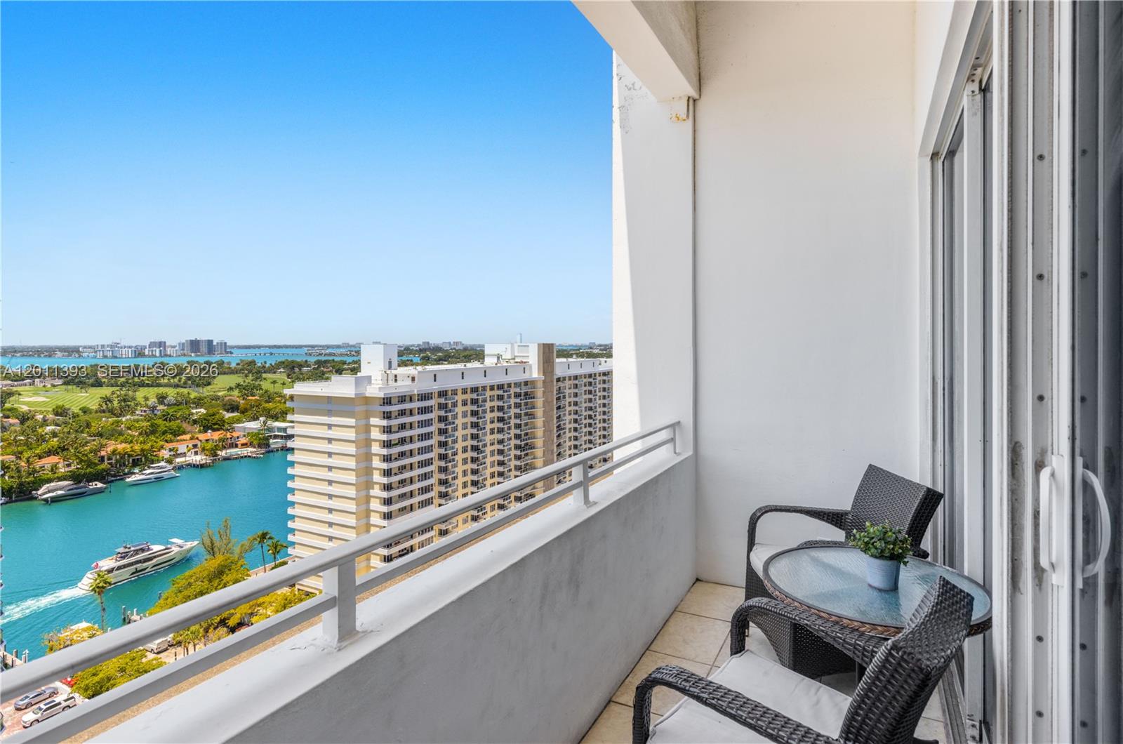 A balcony with two chairs and a small table overlooks a canal and city buildings — 5445 Collins Ave, Miami Beach FL 33140, MIAMI BEACH, FL