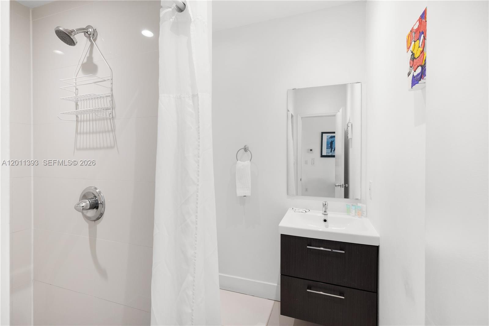This bathroom features a walk-in shower with a white curtain, a vanity, and a mirror — 5445 Collins Ave, Miami Beach FL 33140, MIAMI BEACH, FL