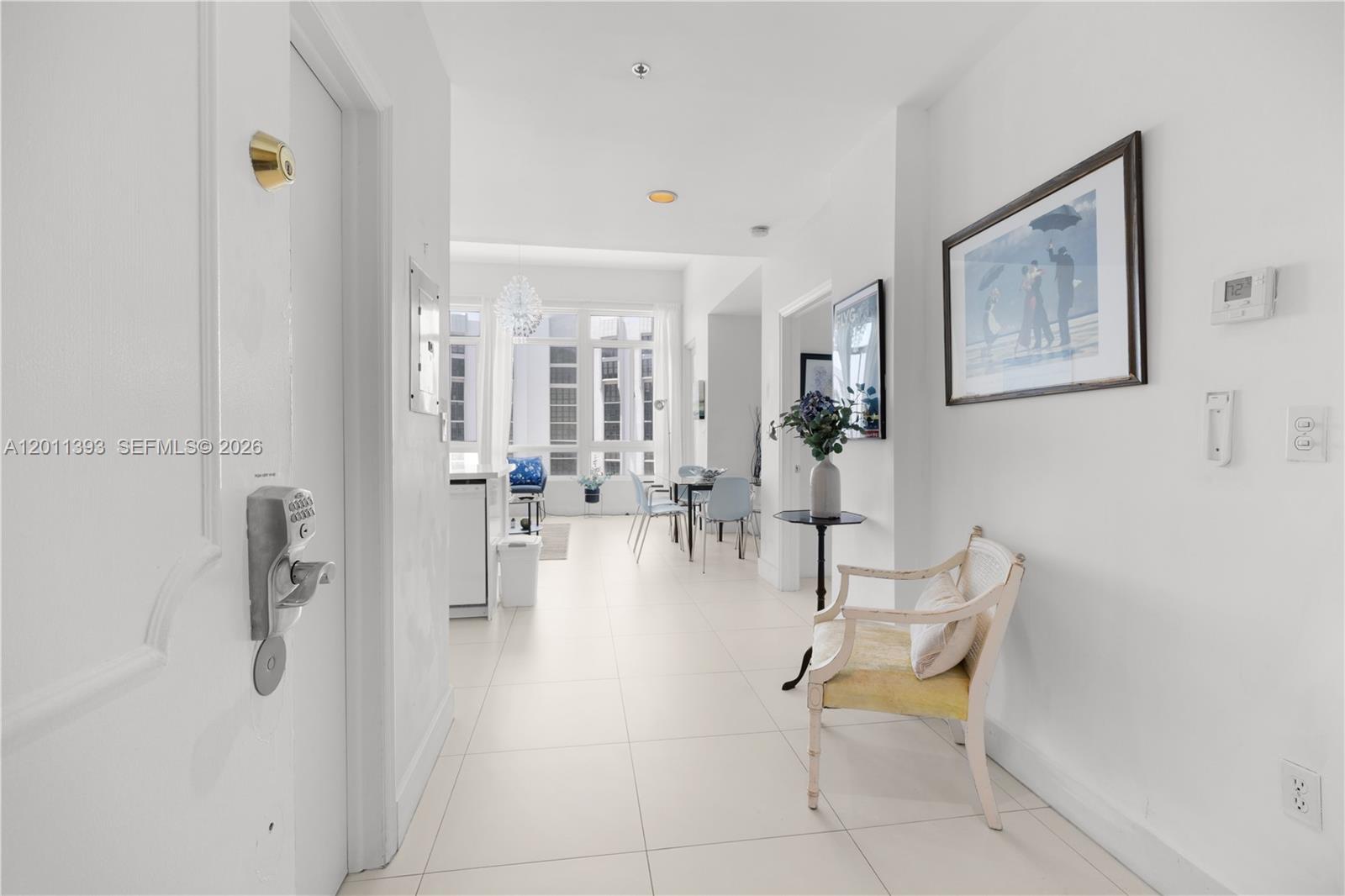 A white-walled entryway features a light-colored chair, tiled floors, and a view into a living area — 5445 Collins Ave, Miami Beach FL 33140, MIAMI BEACH, FL
