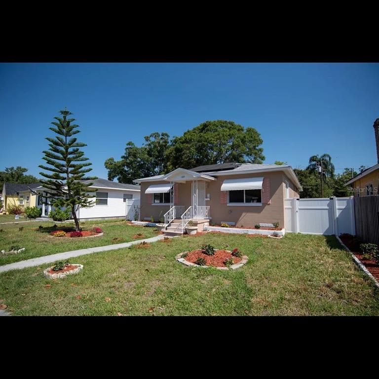 A single-story tan house with a white fence, a front porch, and a tall pine tree — 1329 34TH AVENUE N, ST PETERSBURG, FL