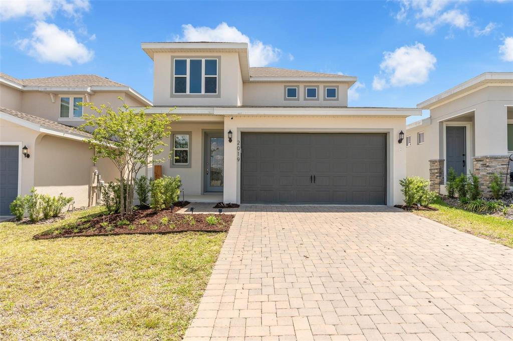 A two-story suburban house features a paved driveway, a gray garage door, and light-colored siding — 2019 SUNSHINE PEAK DRIVE, MINNEOLA, FL