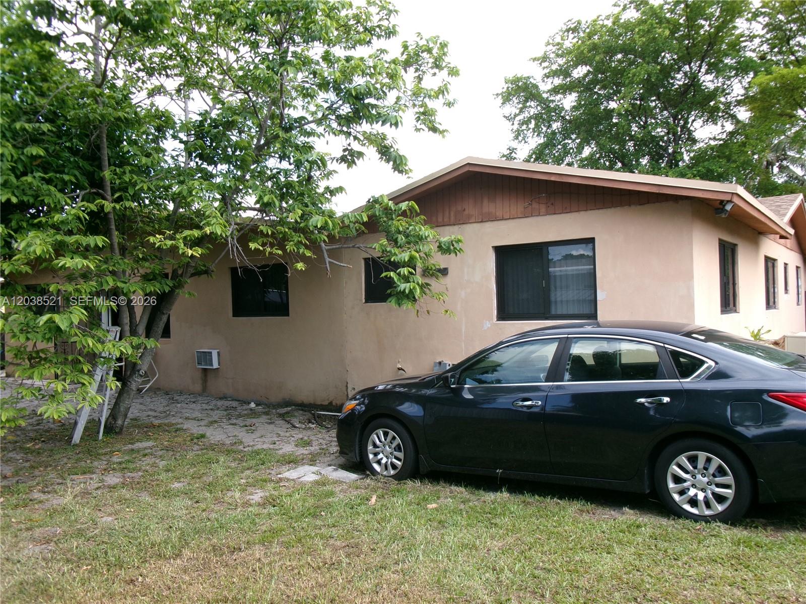 A dark sedan is parked on the grass in front of a tan stucco house — MIAMI, FL