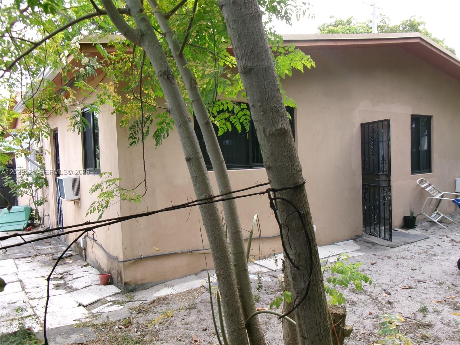 The exterior of a tan stucco house features a metal security door and window screens — MIAMI, FL