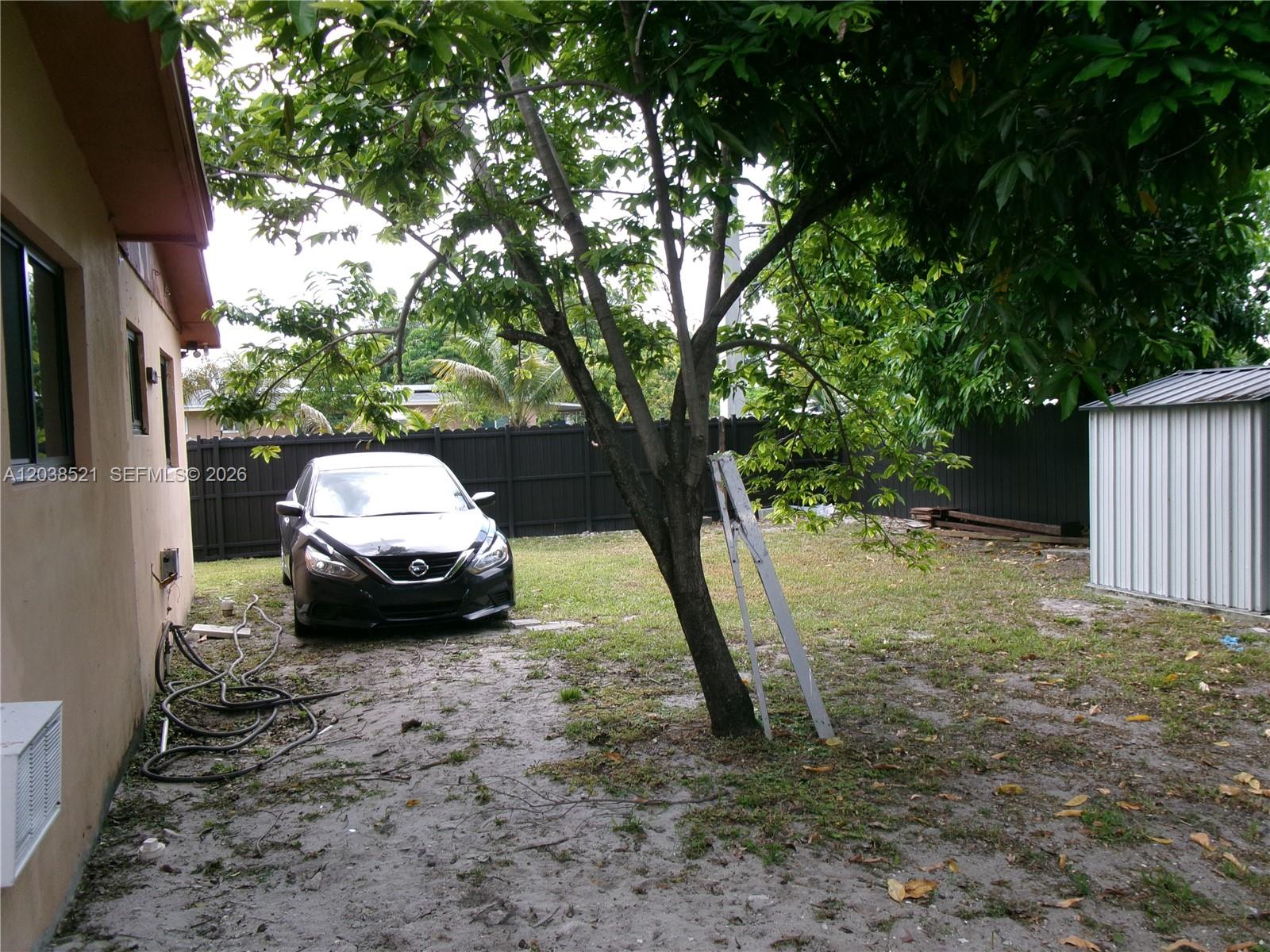 A black car is parked in a backyard with a tree and a metal shed — MIAMI, FL